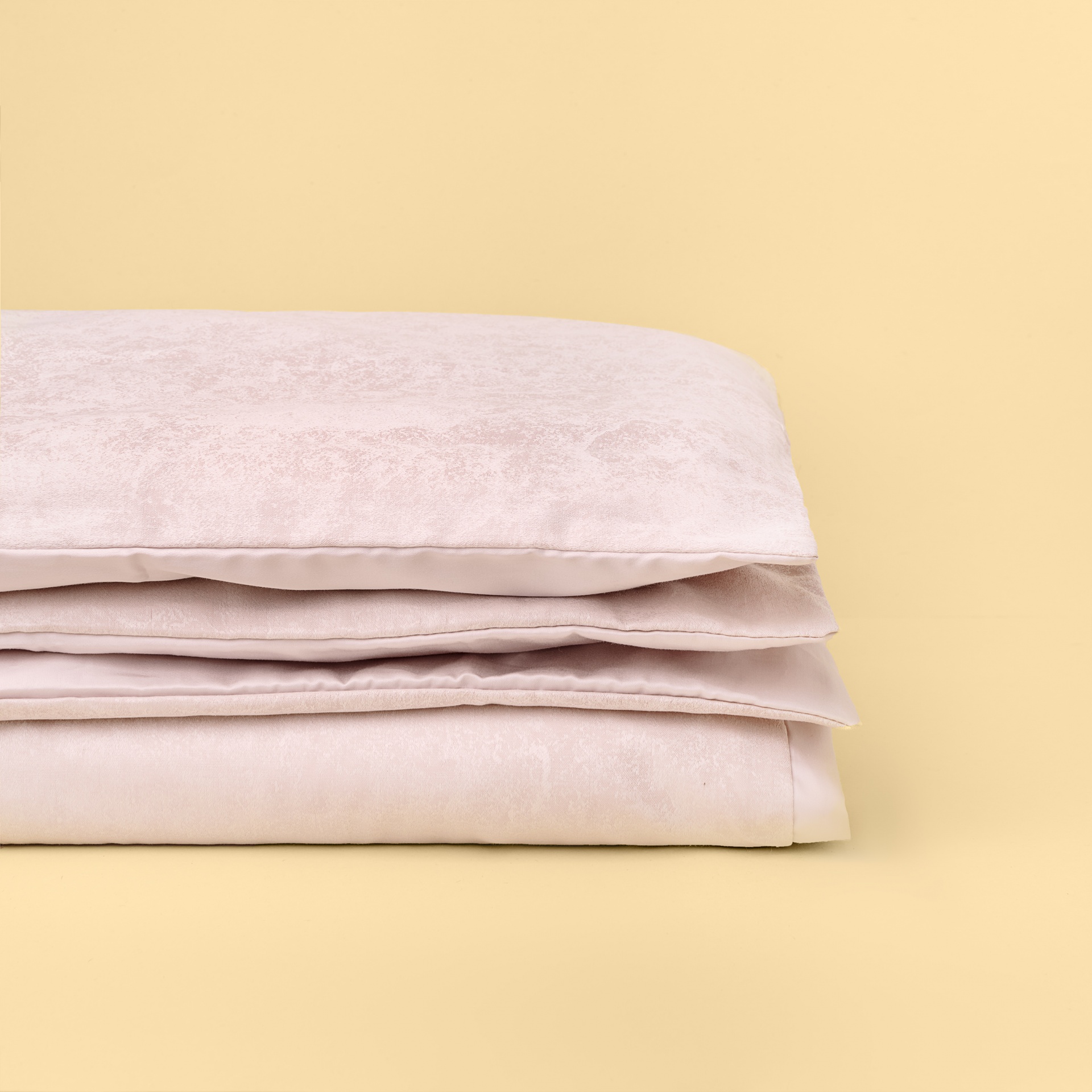 Conjunto de roupa de cama rosa claro dobrado sobre superfície amarela.