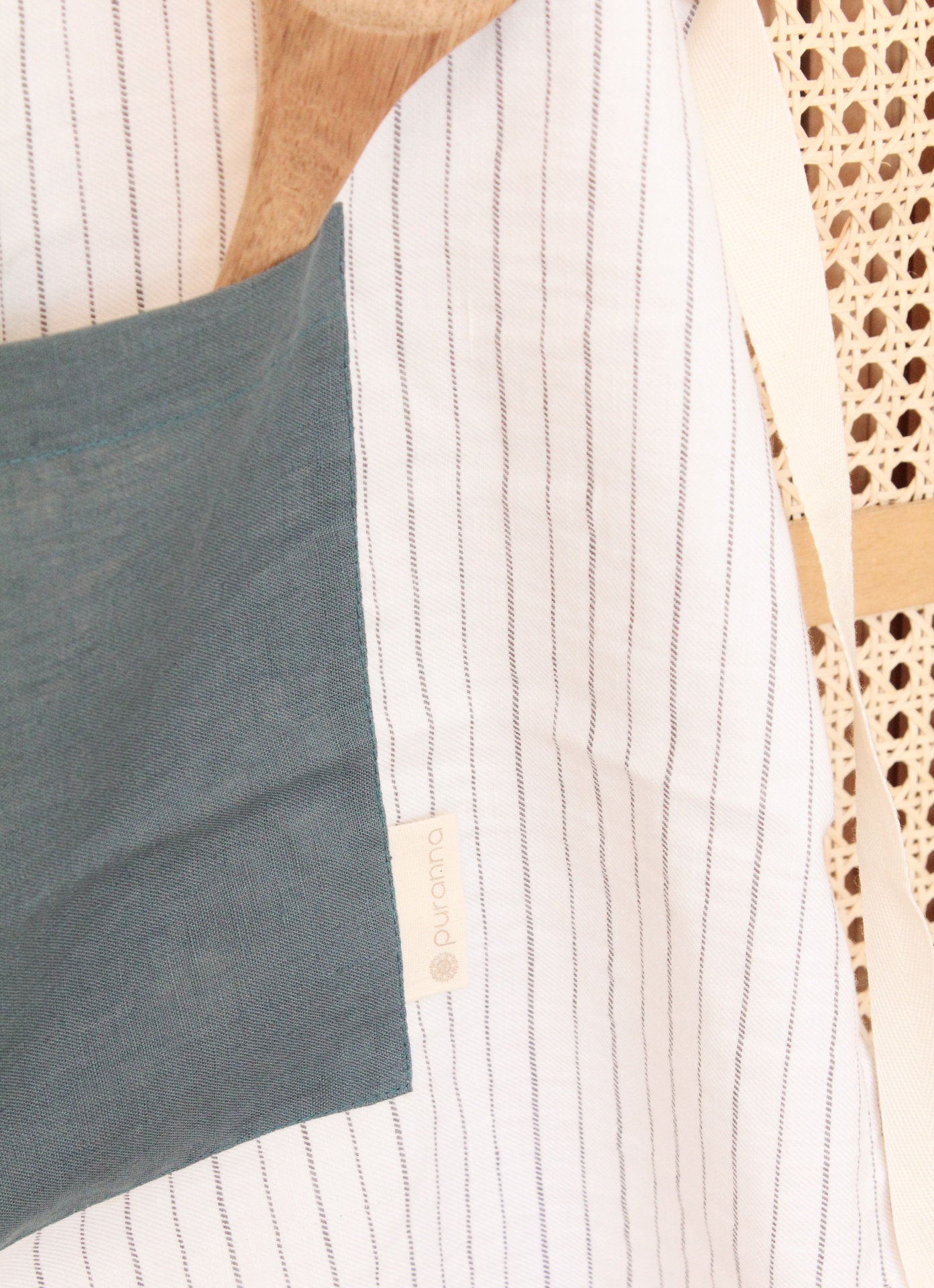 Avental branco com riscas e bolso cinzento escuro com espátula de madeira