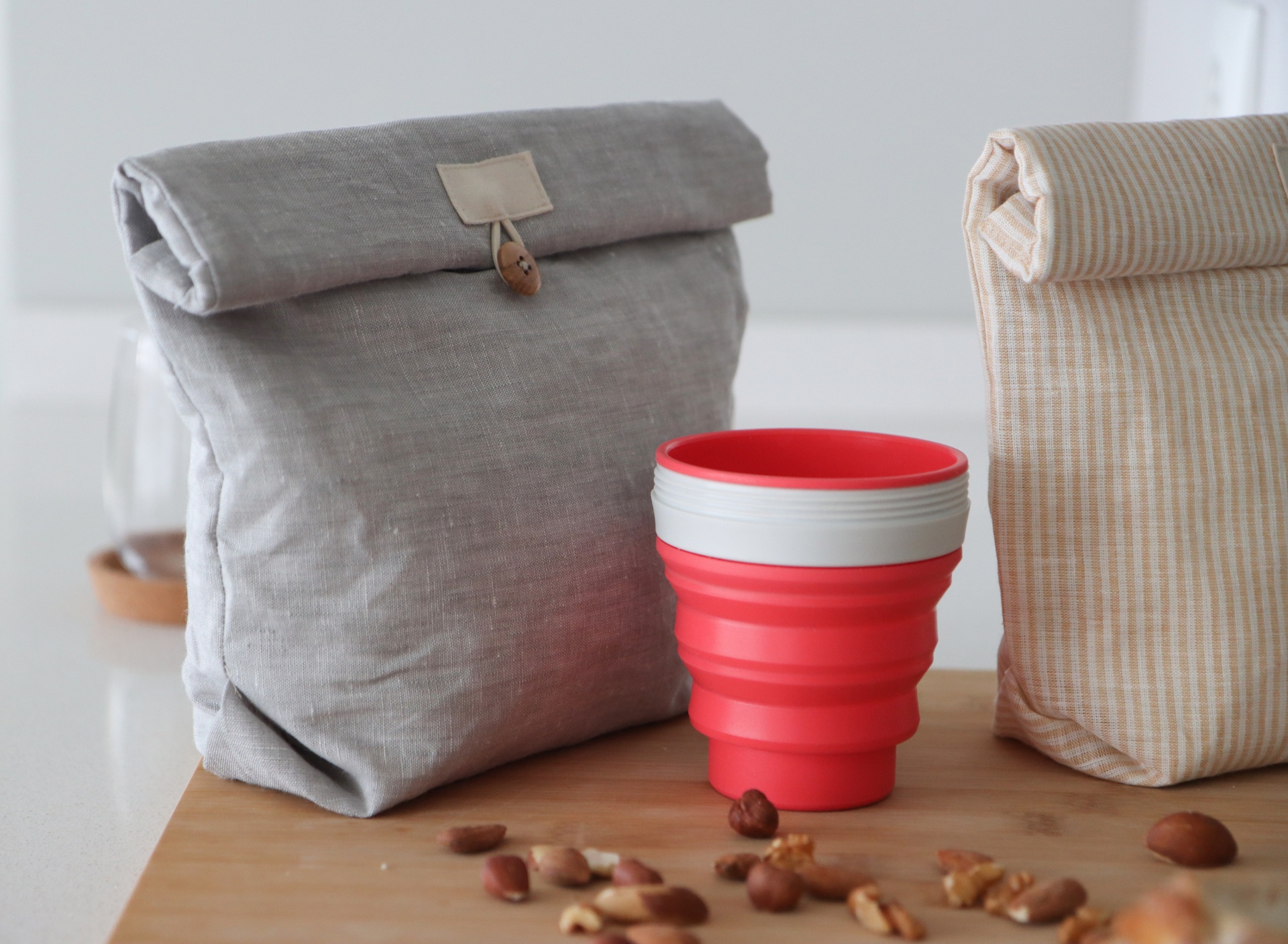 Sacos de almoço em tecido e copo de silicone vermelho dobrável numa mesa com nozes