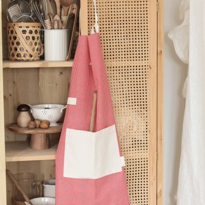 Avental vermelho com bolso branco pendurado em armário de palhinha