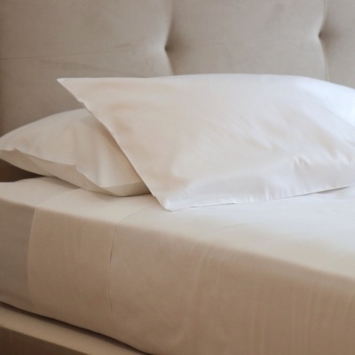 Conjunto de cama branco com almofadas e lençóis sobre colchão e cabeceira estofada bege.