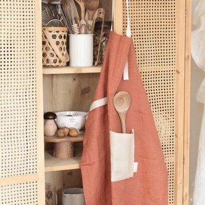 Avental terracota pendurado em armário de madeira com utensílios de cozinha.