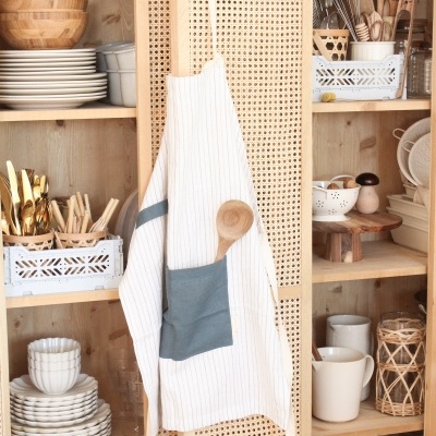 Armário de madeira com pratos, tigelas, canecas e avental pendurado