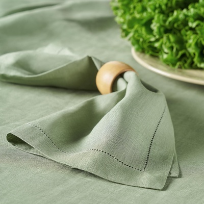 Guardanapo de tecido verde claro com argola de madeira sobre mesa com toalha igual e prato com alface