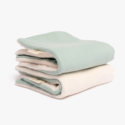Duas mantas dobradas verde claro e bege empilhadas em fundo branco