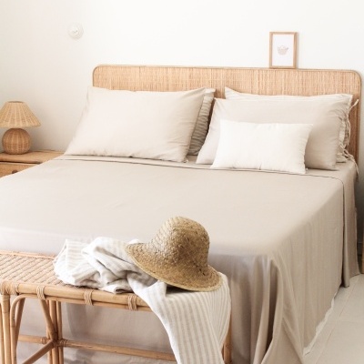 Quarto com cama de casal, cabeceira e banco em rattan, roupa de cama bege, chapéu de palha e manta branca