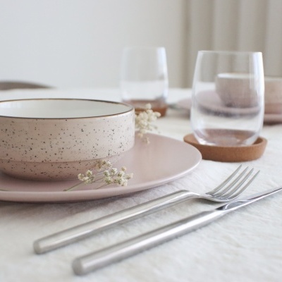 conjunto de loiça bege e rosa claro com copos de vidro e talheres numa mesa com toalha branca