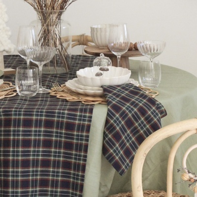 Mesa posta com toalha verde clara e caminho de mesa xadrez, pratos brancos e copos de vidro.