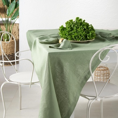 Mesa com toalha verde, prato com alface e cadeiras brancas em ambiente minimalista
