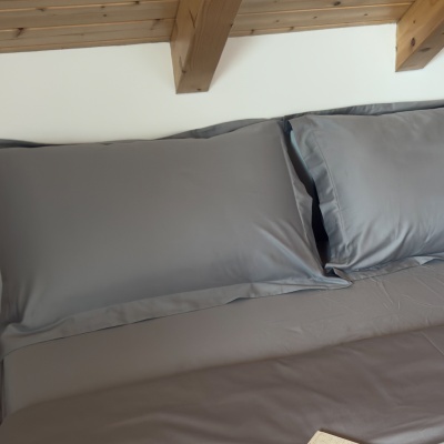 Conjunto de cama cinzento com fronhas sobre cama sob teto de madeira clara