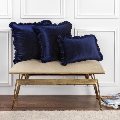 Almofadas de veludo azul escuro com bordas franzidas sobre banco estofado bege com estrutura dourada