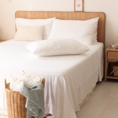 Cama com roupa de cama branca e acessórios em rattan num quarto claro