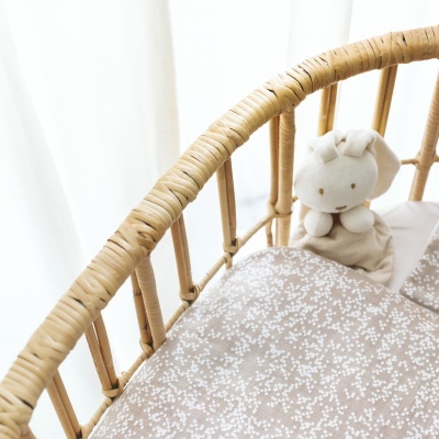 Berço de bebé em verga com colcha bege estampada e boneco de peluche branco.