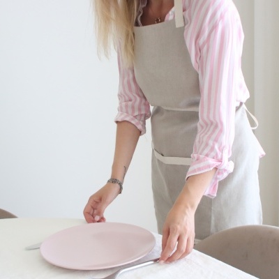 Pessoa a colocar prato rosa numa mesa com toalha branca