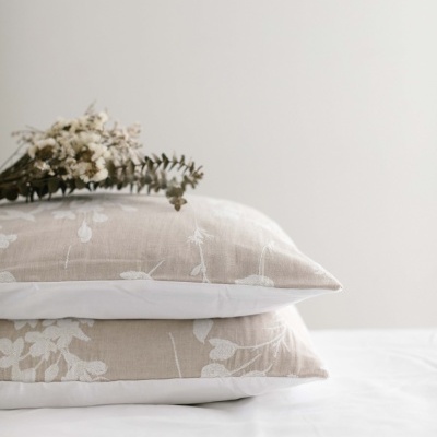 Almofadas com fronhas bege e branca com padrão floral, e flores secas em cima