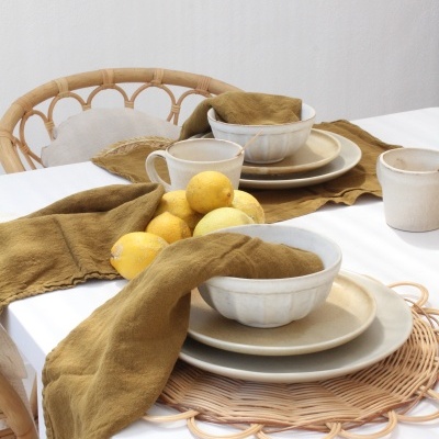 Mesa posta com louça bege, guardanapos verdes e limões sobre mesa branca