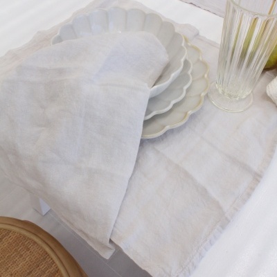 Mesa posta com pratos brancos em camadas e guardanapo bege, copos transparentes, cadeira de madeira e rattan.