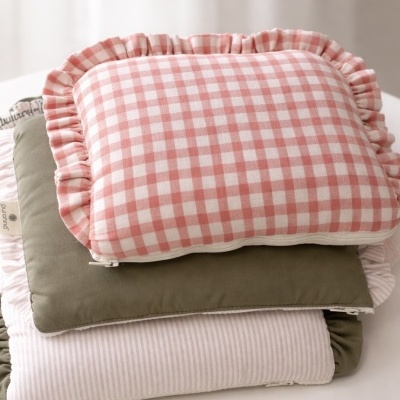 Três almofadas empilhadas em tons rosa, branco e verde-oliva com diferentes padrões e babados.