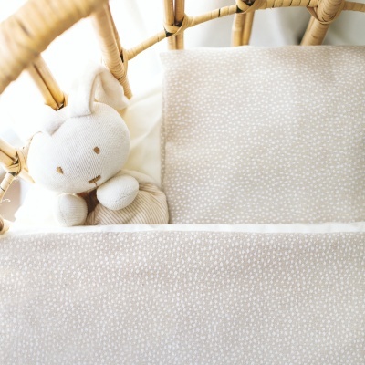Berço de vime com urso de pelúcia e roupa de cama bege com padrão branco