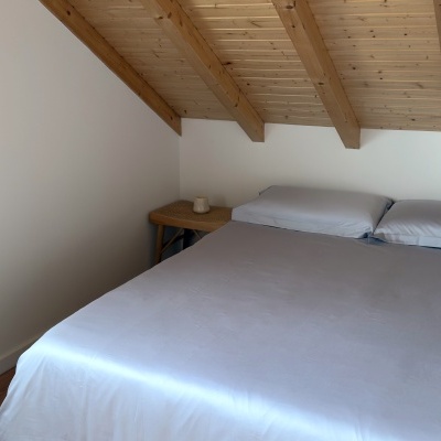 quarto com cama de casal branca e teto de madeira inclinado