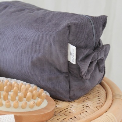 Almofada cinzenta escura com etiqueta Puravida sobre rattan, ao lado de escova de madeira