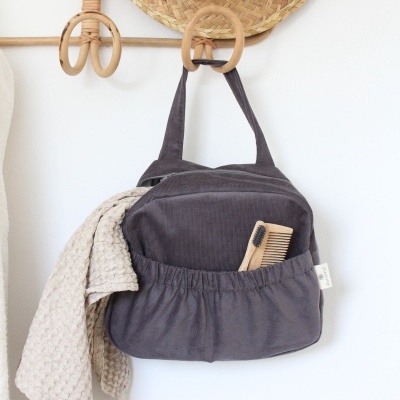 Bolsa cinzenta com bolso frontal elástico pendurada com pano bege e utensílios de madeira