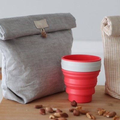 Sacos de almoço em tecido e copo de silicone vermelho dobrável numa mesa com nozes