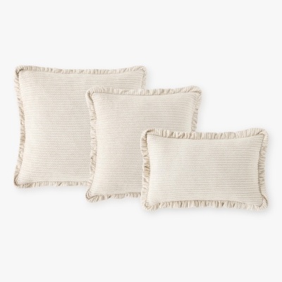 Três almofadas bege claro tricotadas com franjas numa disposição sobre fundo branco