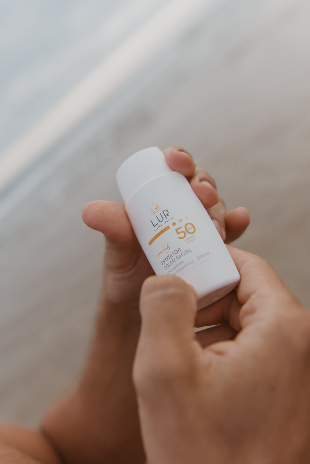 Protetor Solar Facial SPF 50 Frasco branco de protetor solar facial LUR FPS 50 visto de perto nas mãos de uma pessoa