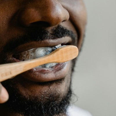 Pessoa a escovar os dentes com escova de madeira e pasta de dentes espumosa