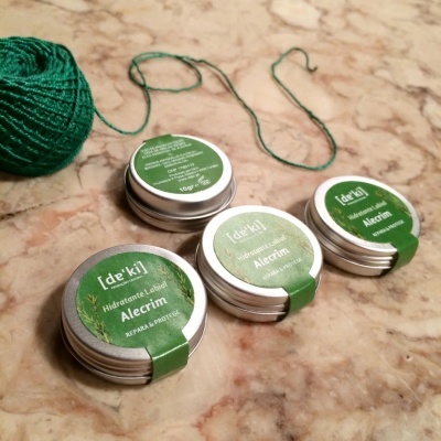 Latas pequenas de hidratante labial Alecrim com rótulos verdes sobre mármore