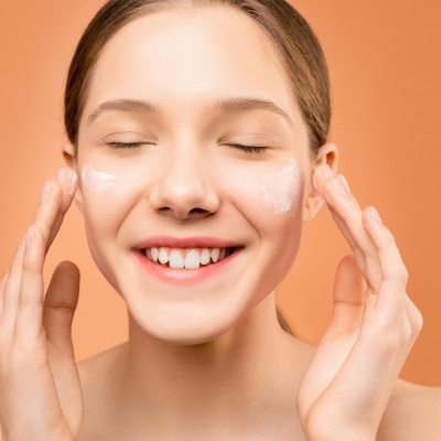 Mulher aplicando creme nas bochechas com fundo laranja
