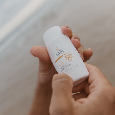 Frasco branco de protetor solar facial LUR FPS 50 visto de perto nas mãos de uma pessoa