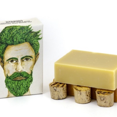 Sabonete tradicional para lavar barba com embalagem ilustrada, e barra de sabão bege sobre suporte.