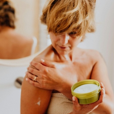 Mulher a aplicar creme com recipiente verde e creme branco