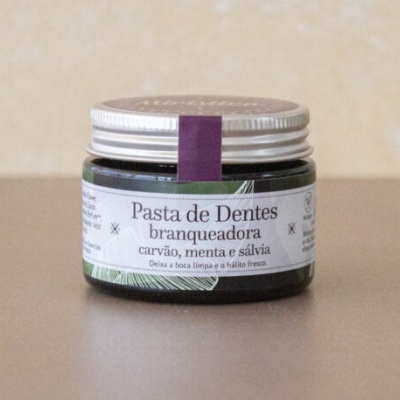 Frasco de pasta de dentes branqueadora com carvão, menta e sálvia sobre superfície castanha