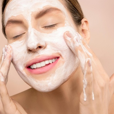 Mulher a aplicar creme facial branco no rosto com fundo cor de rosa