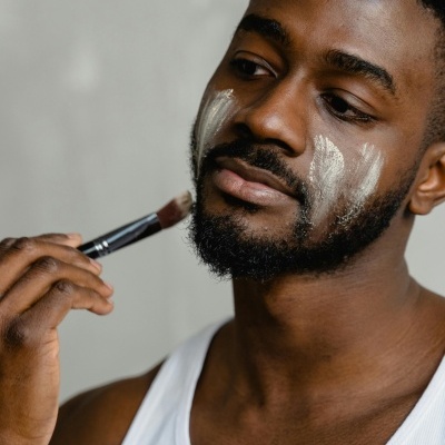 Homem a aplicar creme branco no rosto com pincel