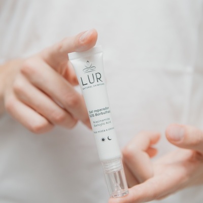 Mãos seguram tubo branco de gel reparador SOS Borbulhas da marca LUR