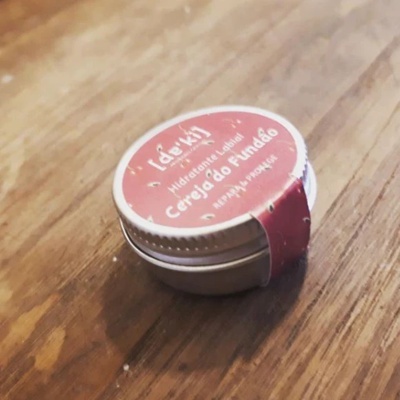 Frasco pequeno com tampa branca e rótulo vermelho com texto branco sobre superfície de madeira.