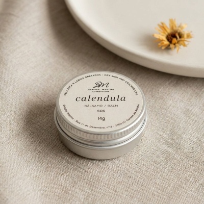 Bálsamo calendula em recipiente metálico prateado sobre tecido bege claro