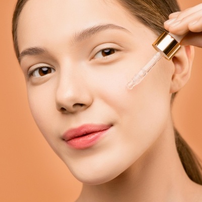 Mulher a aplicar sérum facial com conta-gotas de vidro e tampa dourada