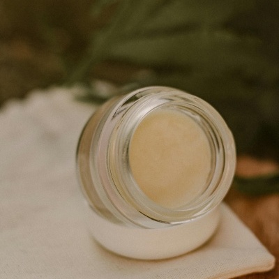 Frasco de vidro com creme amarelo sobre pano branco em madeira