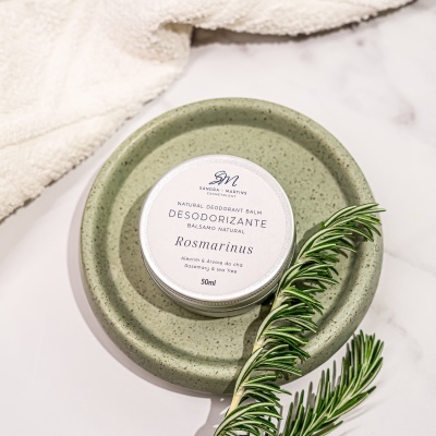 Pote de desodorizante natural Rosmarinus sobre prato verde com ramo de alecrim e toalha creme
