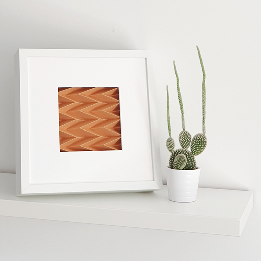 ZIGZAG Mini Wall Art Moldura branca com padrão geométrico laranja em prateleira com vaso branco e cacto verde