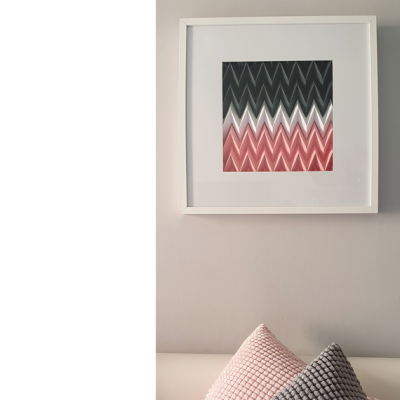 quadro emoldurado branco com padrão ondulado preto, branco e rosa na parede e duas almofadas texturizadas rosa e cinza num sofá claro