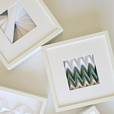 Quadros decorativos brancos com padrões geométricos em relevo e detalhes em verde