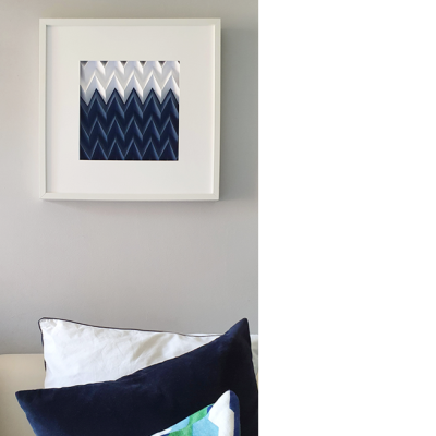 Quadro com padrão branco e azul pendurado na parede cinza acima de almofadas branca e azul.