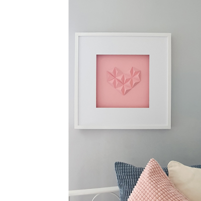 Quadro branco com coração rosa em relevo sobre parede cinzenta e almofadas coloridas