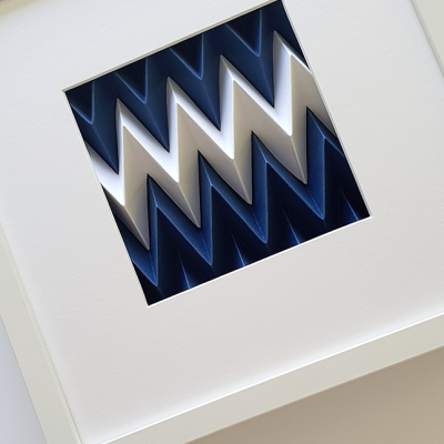 Obra de arte tridimensional com padrão ziguezague azul e branco em moldura branca